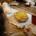Ovenschotel met gegratineerde aardappelpuree en bieslook op een tafelloper met gouden sterren, met brandende kaarsen en wijnglazen.